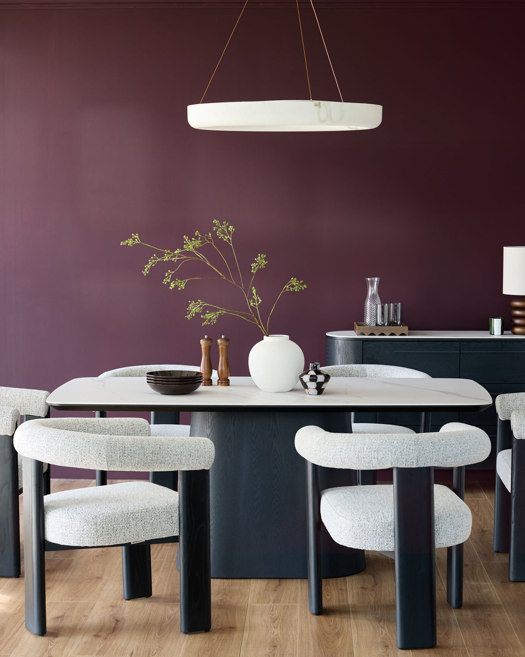 A modern dining set featuring upholstered chairs, a marble-look table, and a sideboard, all under a circular pendant light.