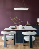 A dining set with a marble-topped table, upholstered chairs and a sideboard, lit by a modern ring pendant light.