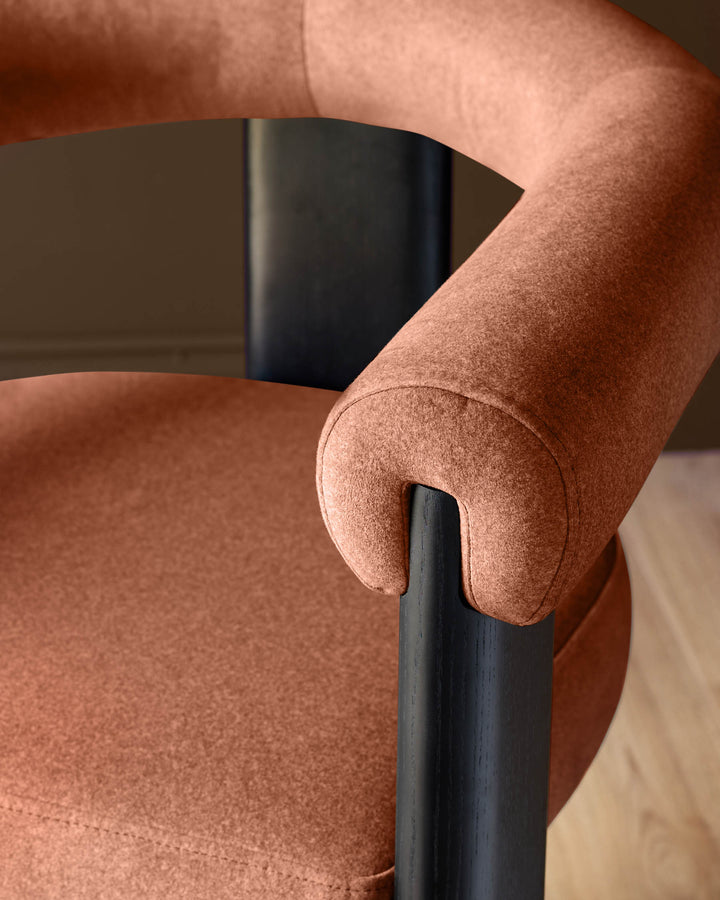 Orion dining chair in toffee-red fabric with black wooden armrest and curved backrest detail, close-up side view.