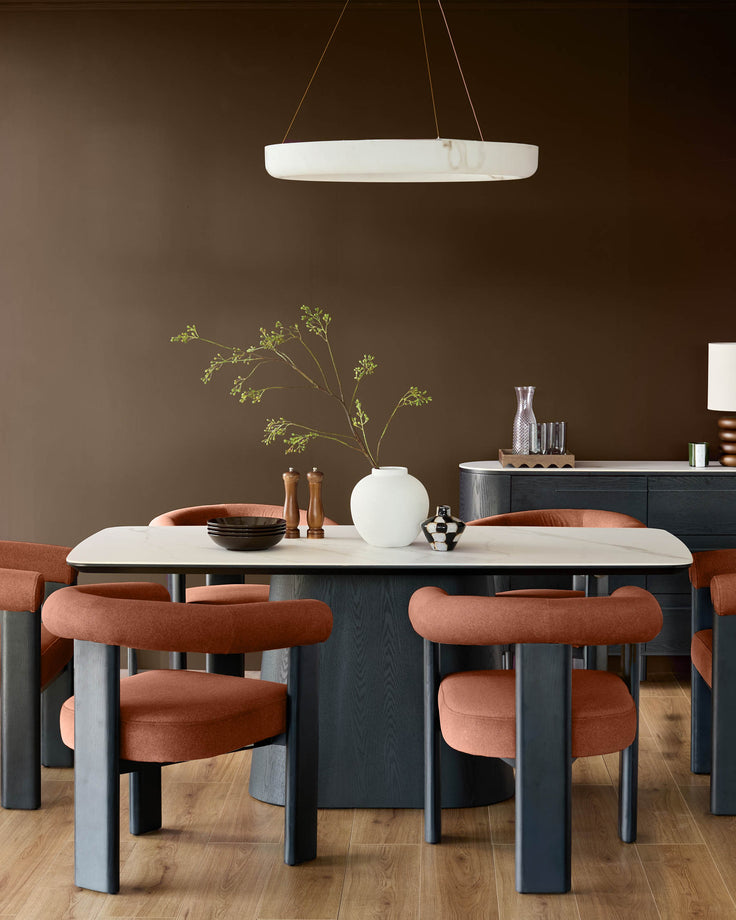 Toffee-red fabric dining chair with curved backrest and cylindrical legs, shown at dining table.
