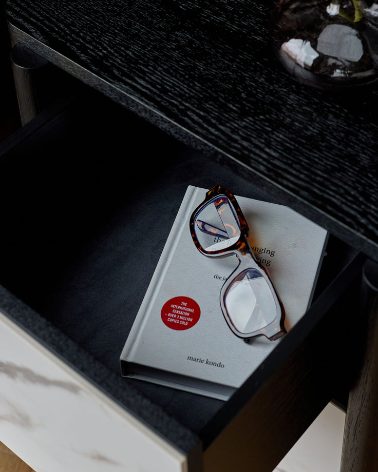 Black ceramic bedside table with a white book and tortoiseshell glasses resting on top.