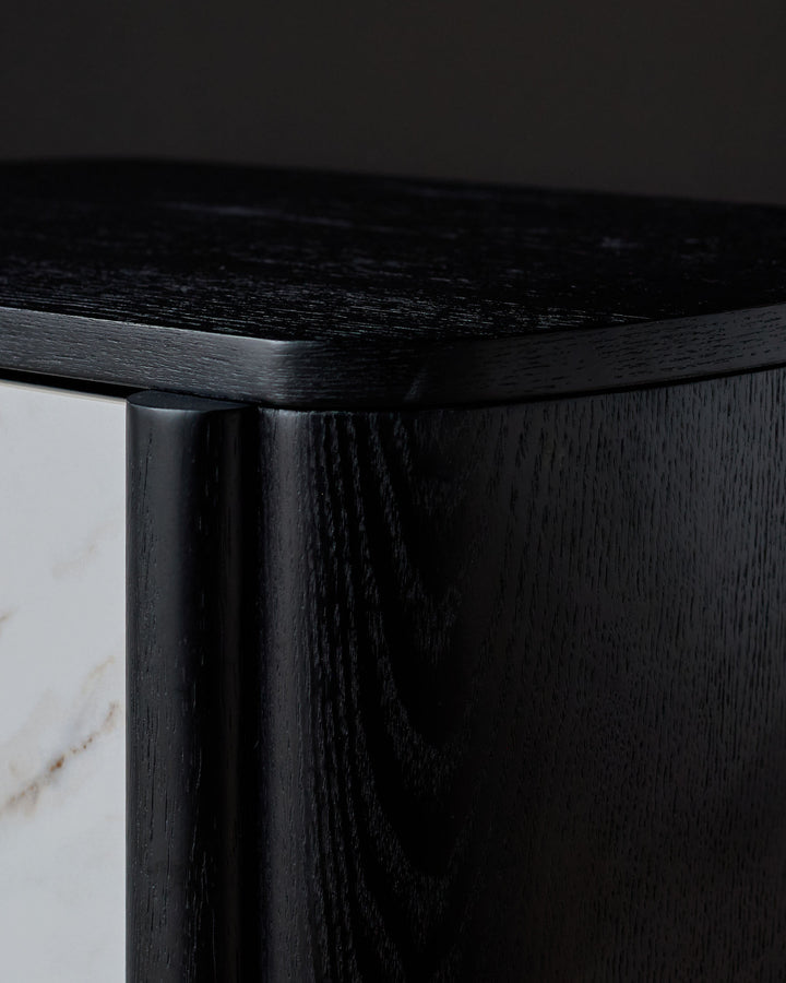 Close-up detail of black wooden bedside table corner showing wood grain texture and white marble drawer front.
