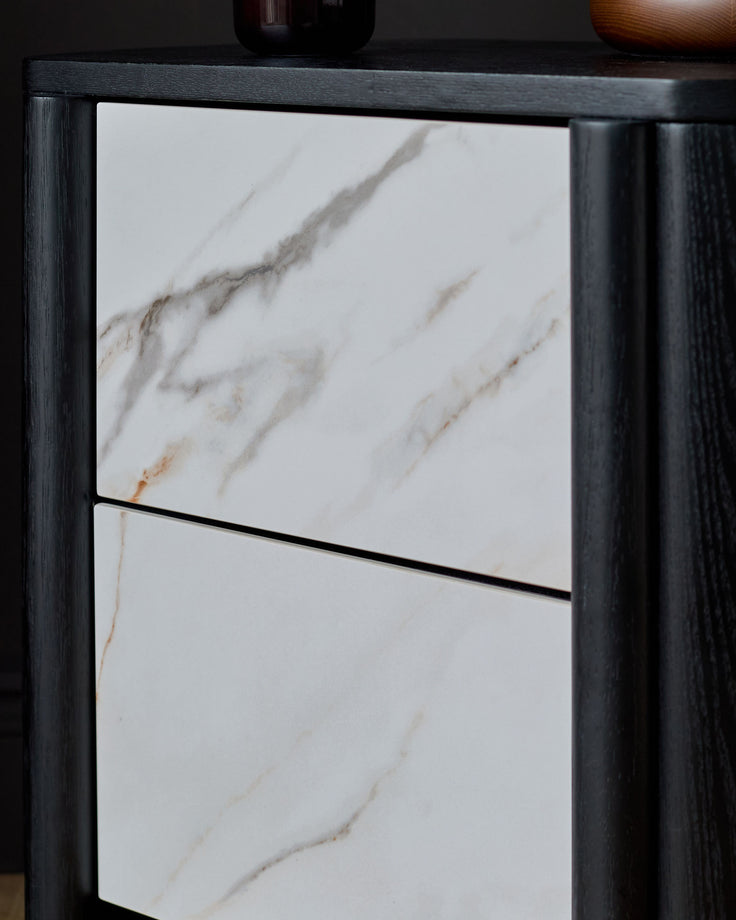 Orlan bedside table with black wooden frame and white marble top with natural veining, drawer front visible.