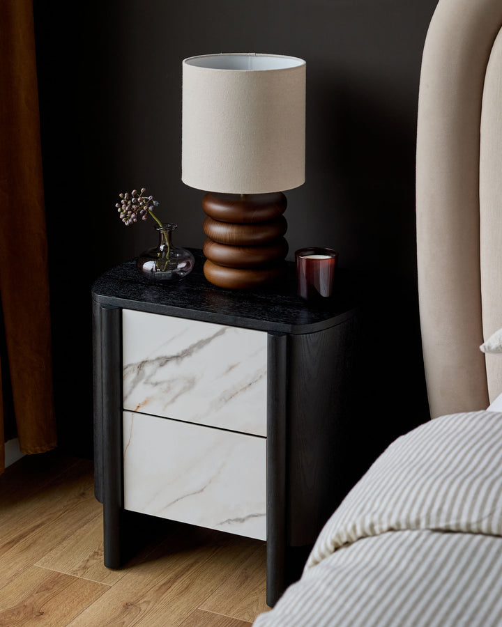 Orlan bedside table with black wooden frame, marble-effect ceramic drawers, and black top surface, styled in a bedroom setting.