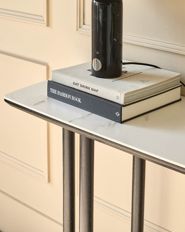 A stylish console table with a marble-effect top, stacked with books and topped with a sleek, black lamp.