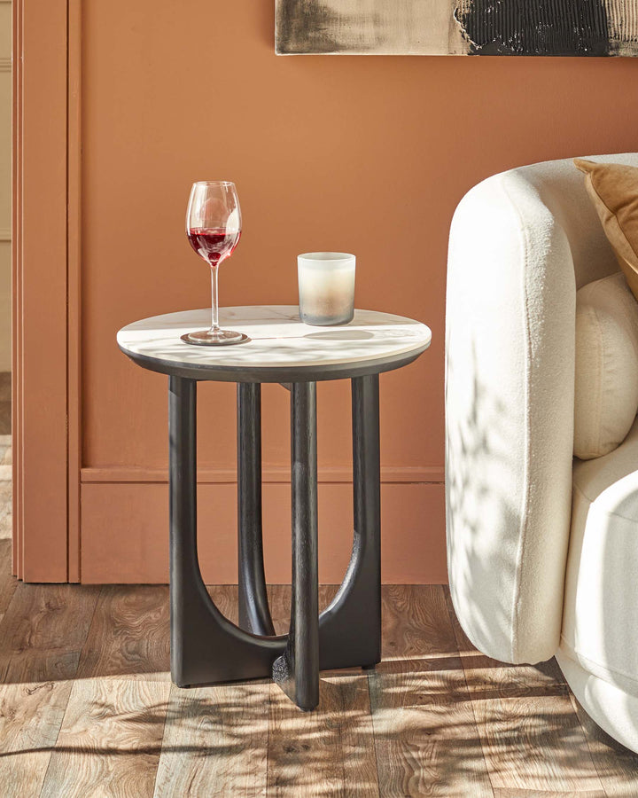 A modern side table with a marble top and dark wood legs, next to a cream coloured sofa.