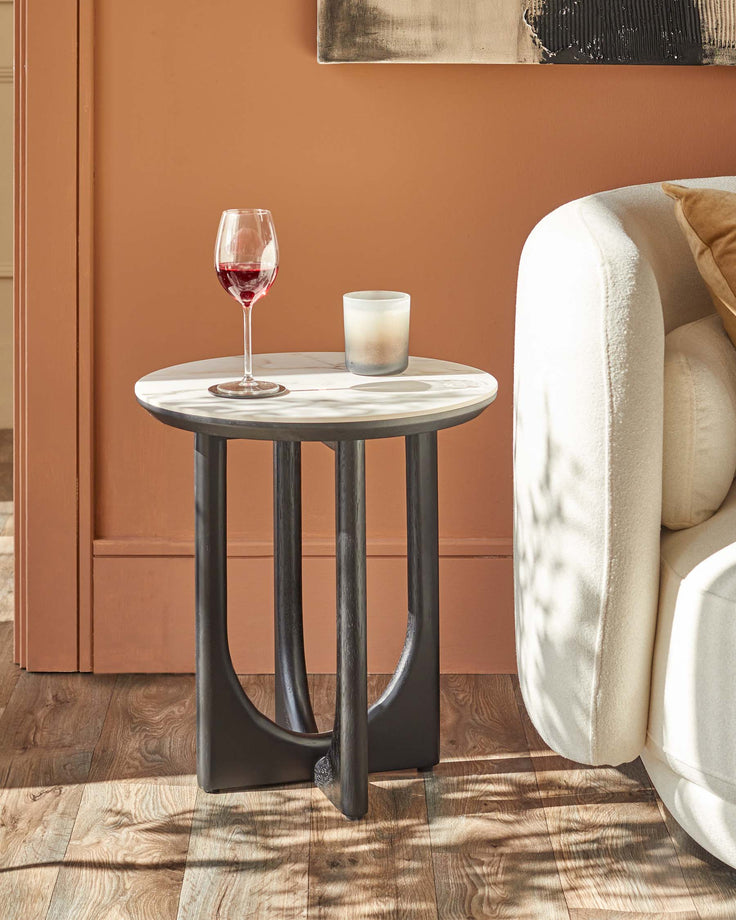 A modern side table with a marble top and dark wood legs, next to a cream coloured sofa.