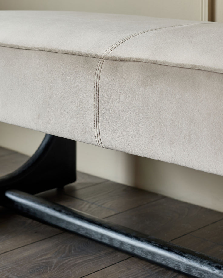 Close-up of a stylish bench with a plush, light-coloured cushion and sleek, dark wood legs, showcasing elegance and modern design.