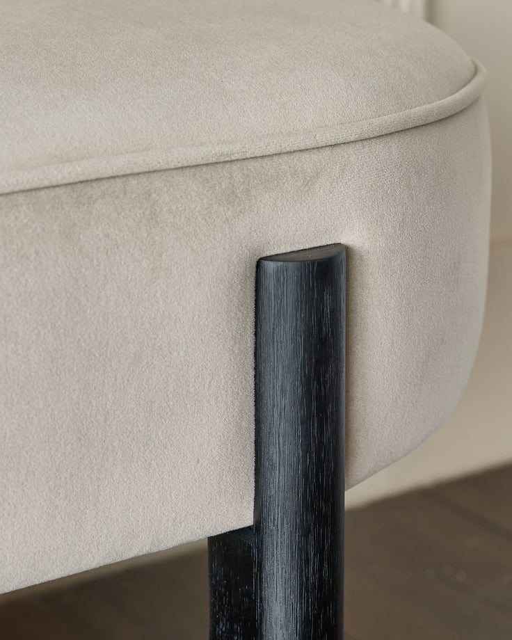 Close-up of a light beige upholstered stool with a dark wood leg, showcasing texture and modern design.