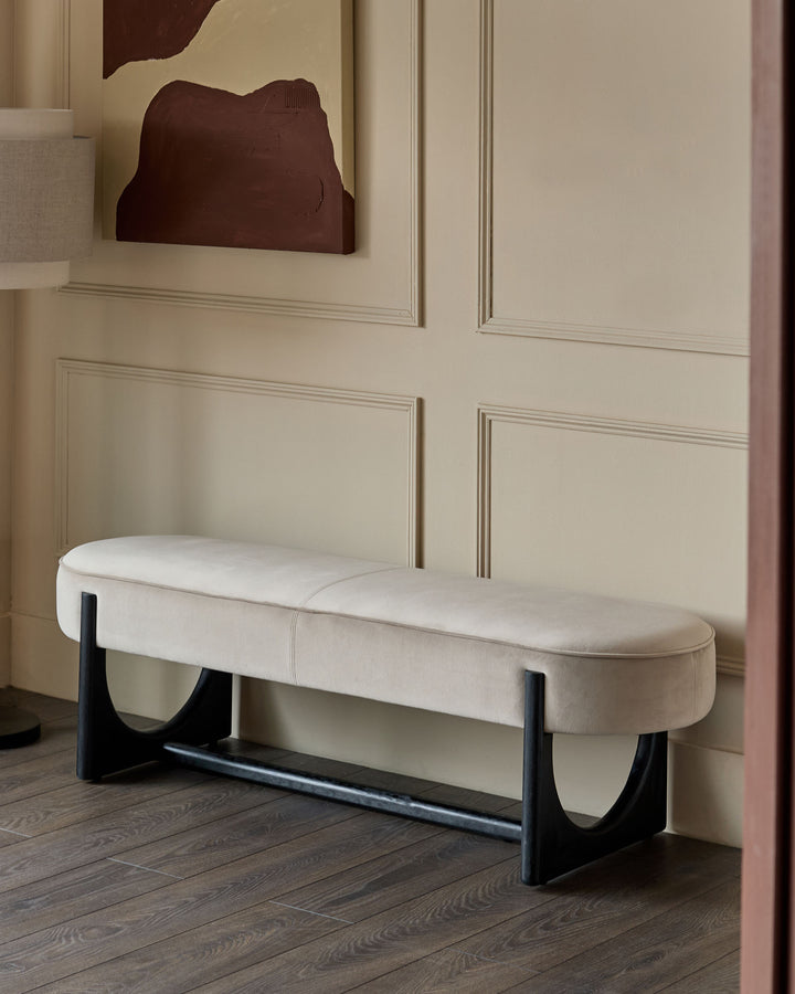 A stylish, upholstered bench with black legs sits against a panelled wall, radiating minimalist sophistication.