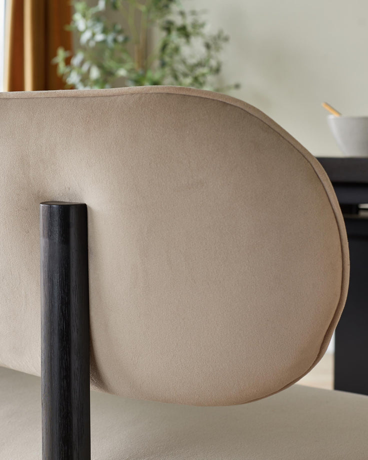 Close-up of a beige upholstered chair with a dark wooden leg. Part of a modern dining set.