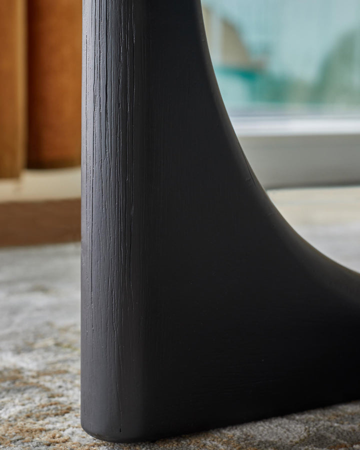 A black, textured furniture leg with curved design detail sits on a grey and brown rug. Window in background.