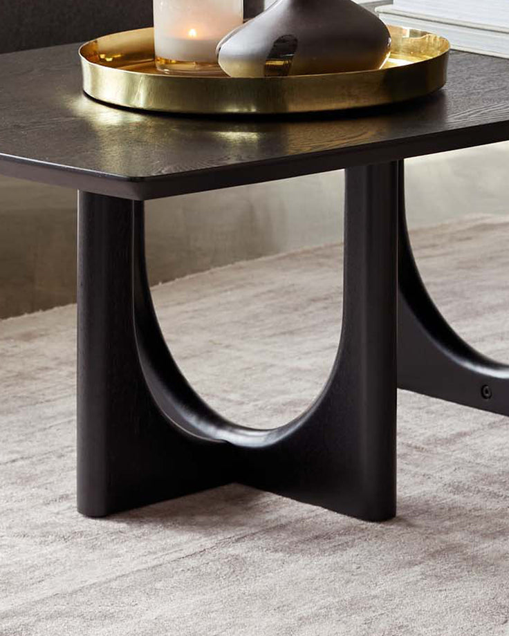 Orlan coffee table in black ash veneer with curved sculptural base and round brass tray top, styled with candle and decor.