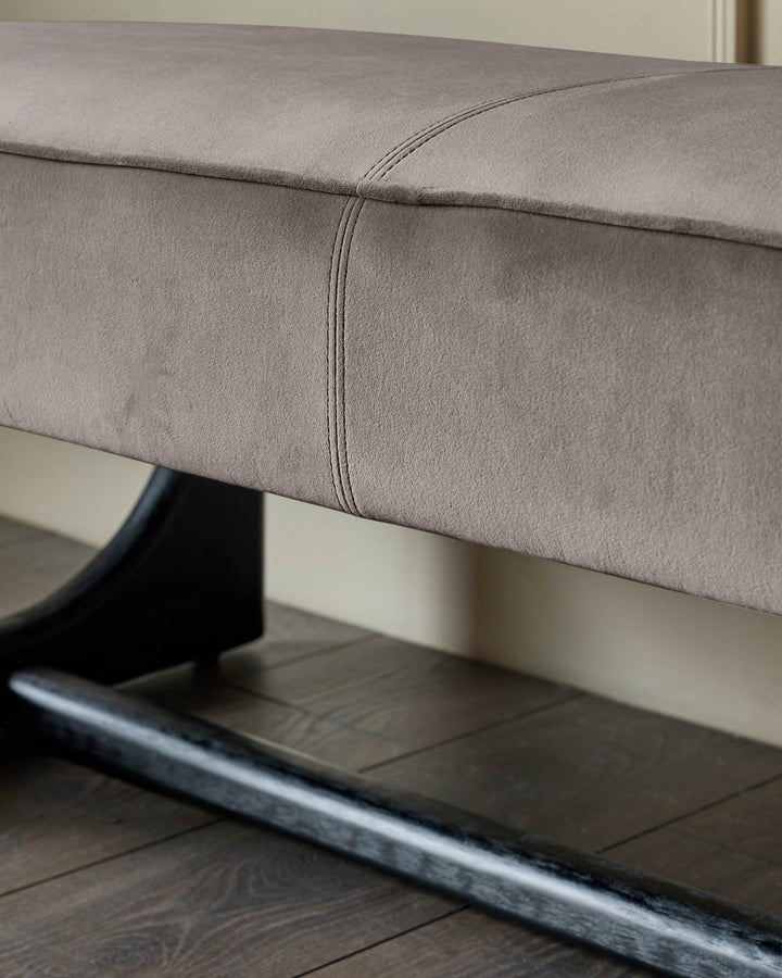 Close up of a contemporary stool with a grey upholstered seat and stylish black wooden legs, resting on a wood floor.