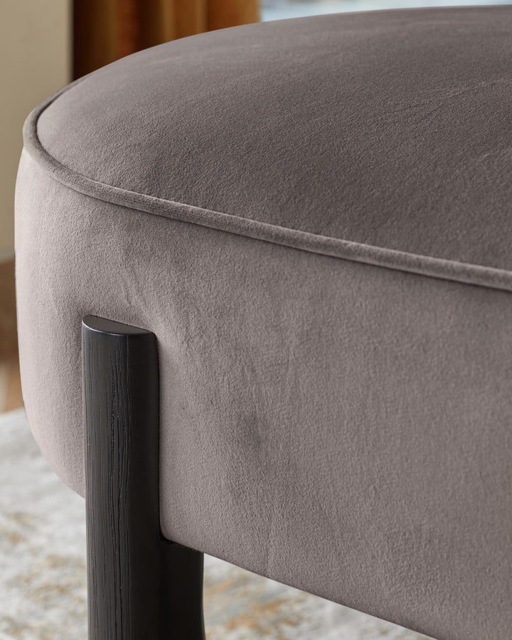 A close-up of a stylish upholstered stool with dark wooden legs, showcasing its soft texture and elegant design.