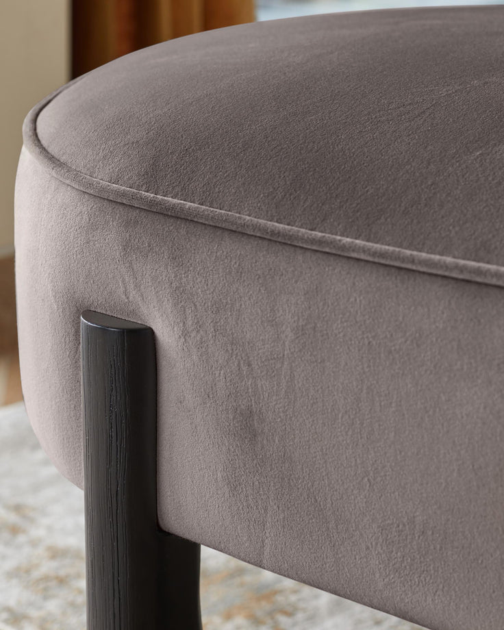 A close-up of a stylish upholstered stool with dark wooden legs, showcasing its soft texture and elegant design.