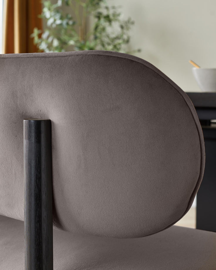 Close-up of a brown upholstered chair with a dark wooden frame, showing its curved back and sleek design.