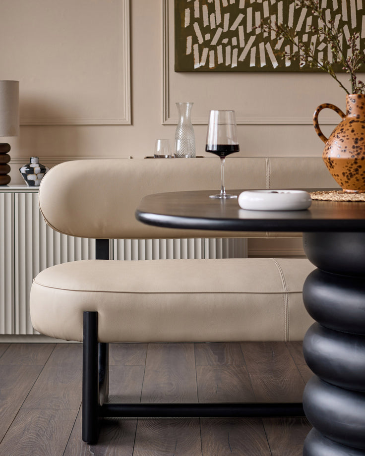 Orlan 3-seating dining bench with backrest in natural faux leather, black metal frame, curved design, styled in modern dining room.