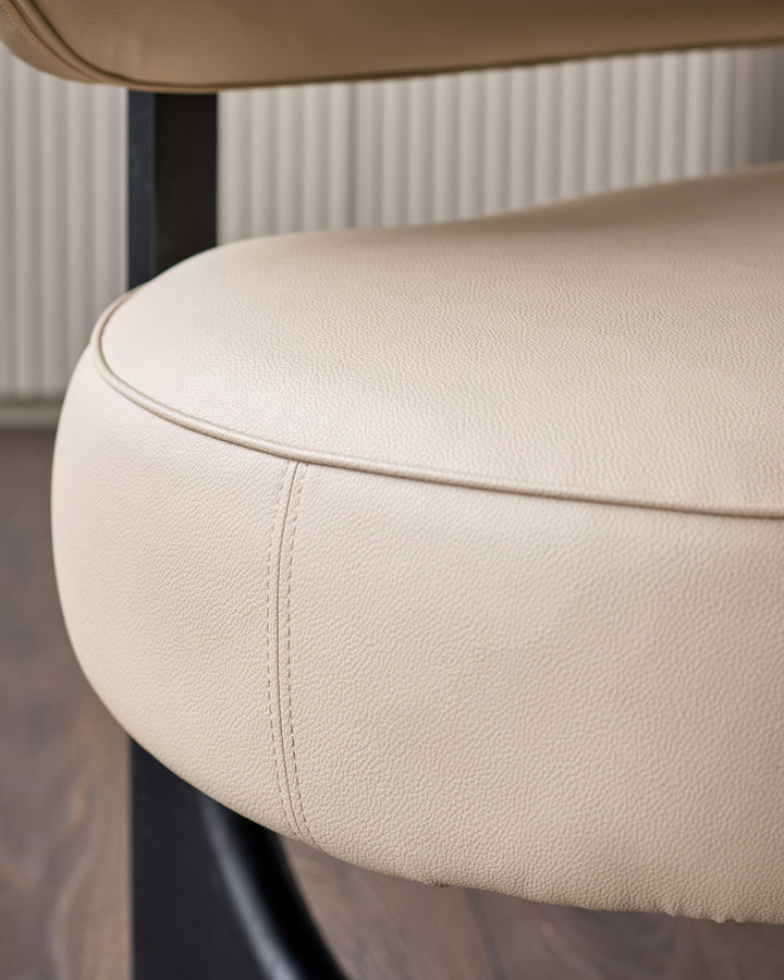 Cream faux leather dining bench with curved backrest, close-up detail of padded seat and stitching.