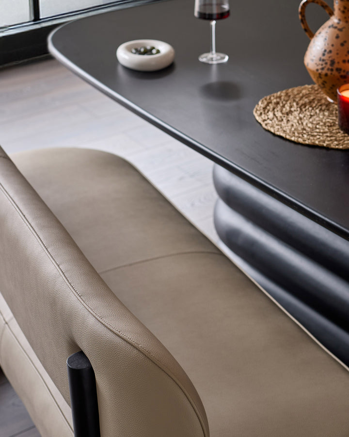 Orlan dining bench with backrest in natural faux leather, shown at table with wine glass and place settings.