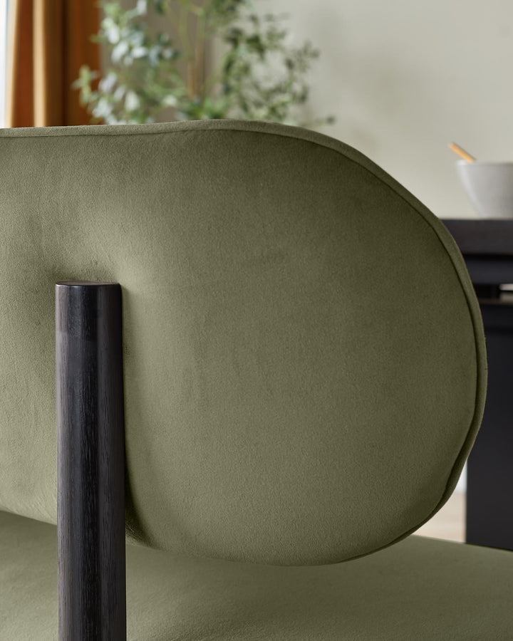 Orlan dining bench with backrest in olive green velvet, showing curved backrest and dark wooden leg detail.