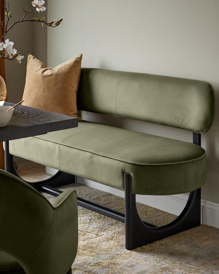 Orlan dining bench with backrest in olive green velvet, black legs, paired with tan cushion and styled with flowers.