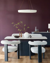 A modern dining set featuring a table with white marble top and 4 upholstered chairs. A pendant light hangs above.