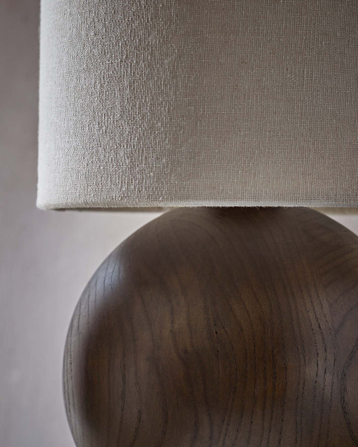 Close up of a lamp with a wooden base and fabric shade, showcasing texture and design details.
