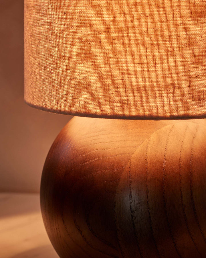 Close-up of a lit table lamp with a wooden base and fabric shade, creating a warm, inviting glow.