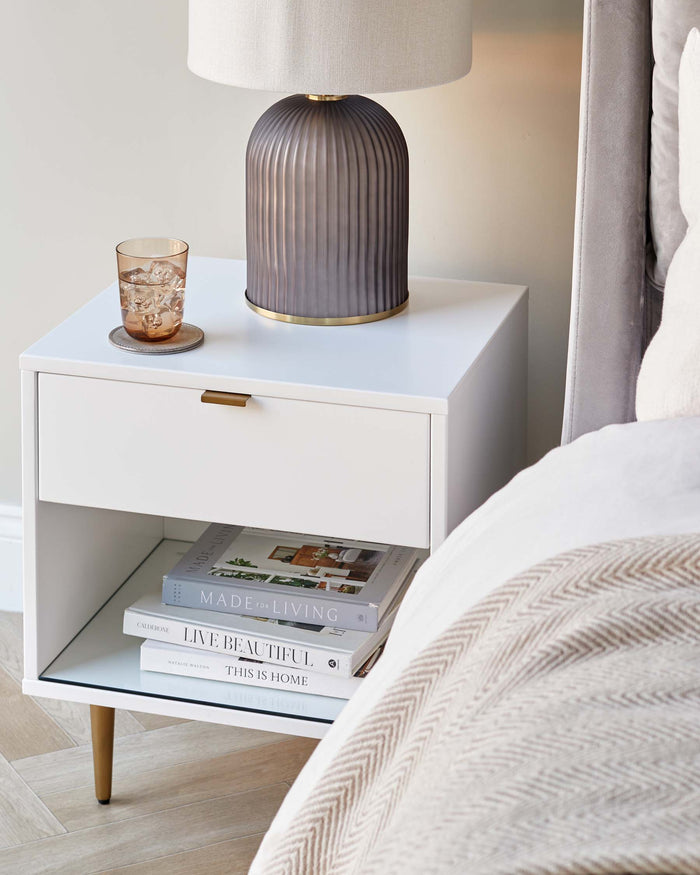 White bedside table with a drawer, shelf, lamp, and books.  Stylish bedroom furniture.