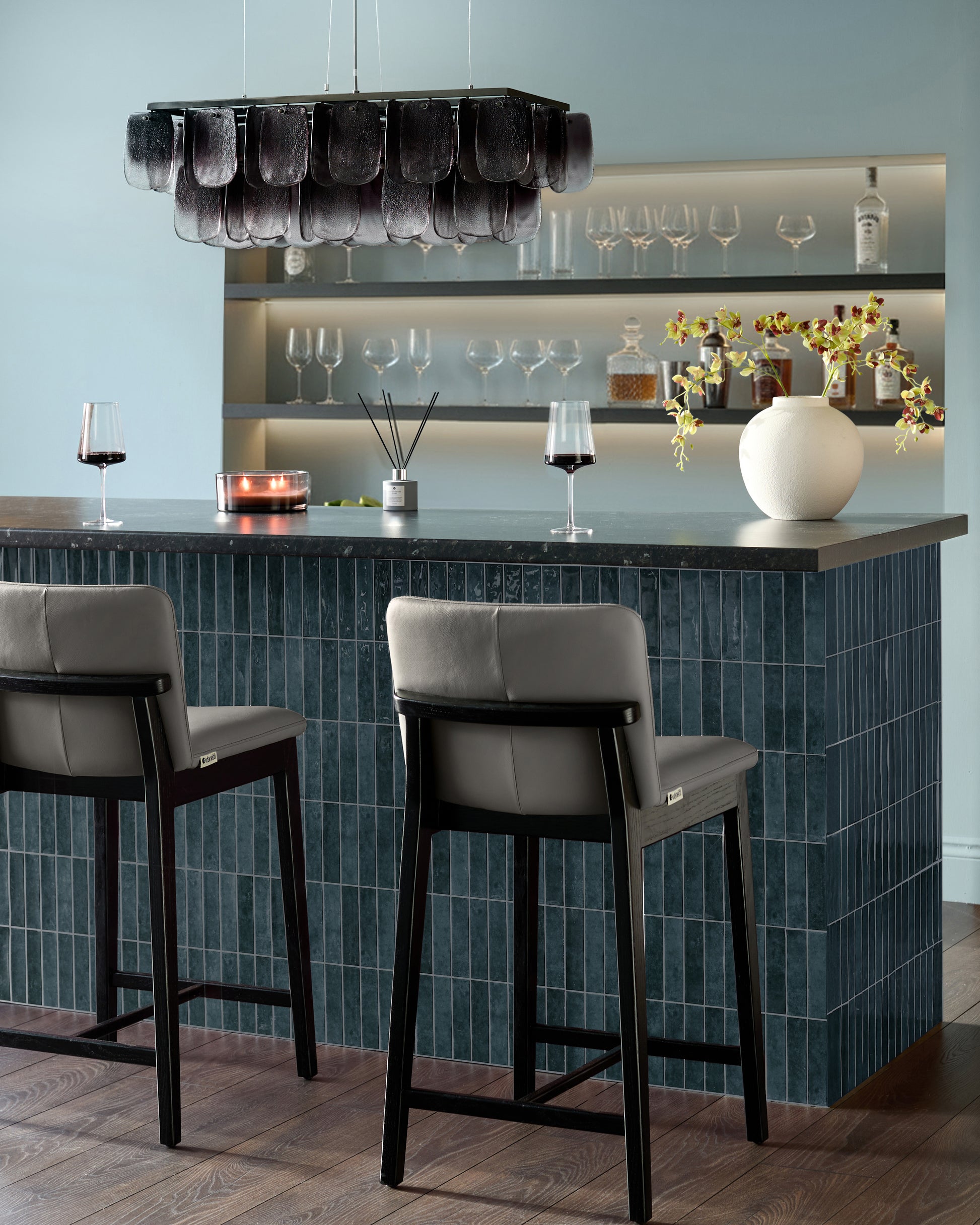 Otis bar stool in dark grey leather with black wooden frame, shown at modern bar counter with light grey upholstered backrest.