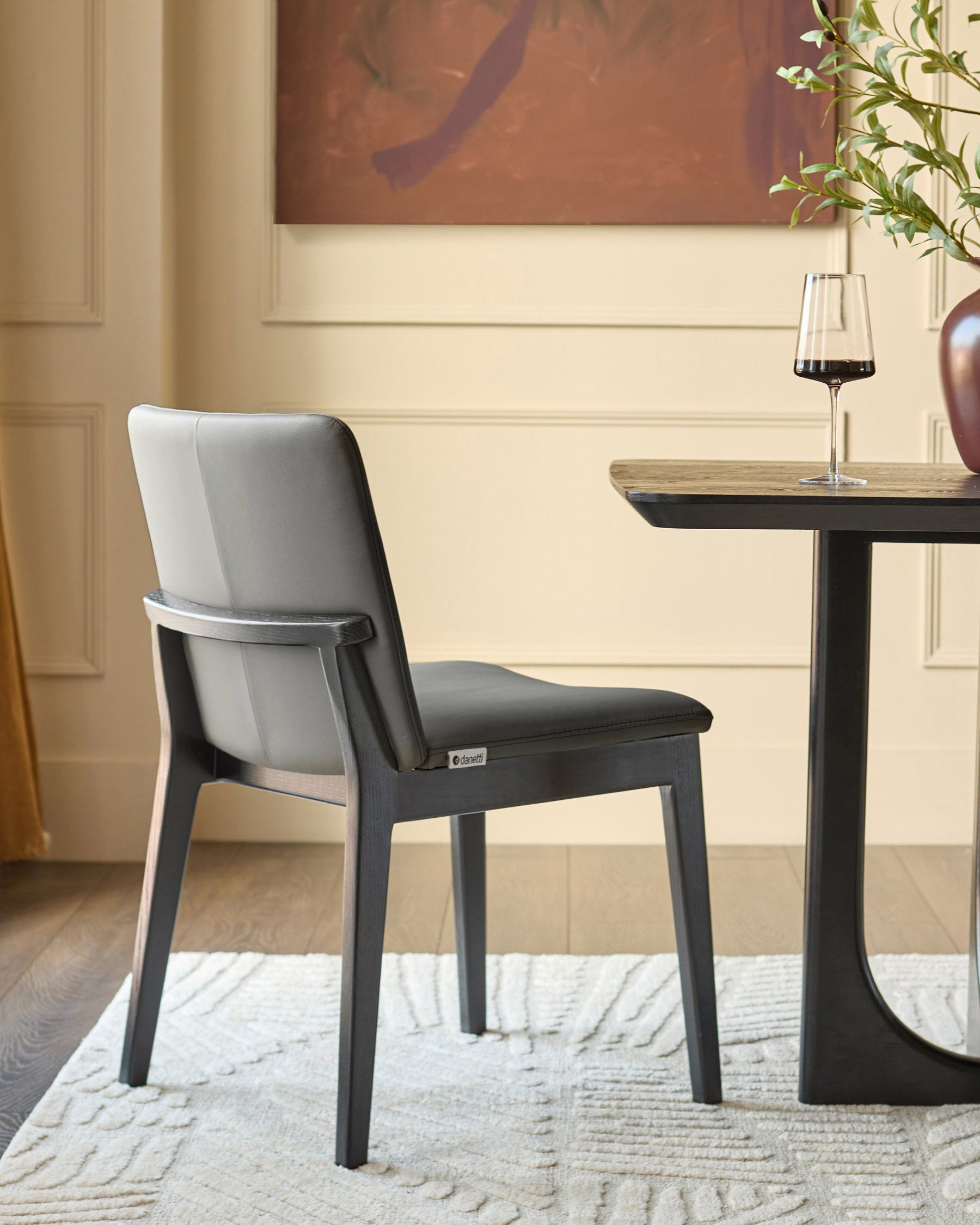 Otis dining chair in dark grey with grey leather backrest, shown at a small table with wine glass.