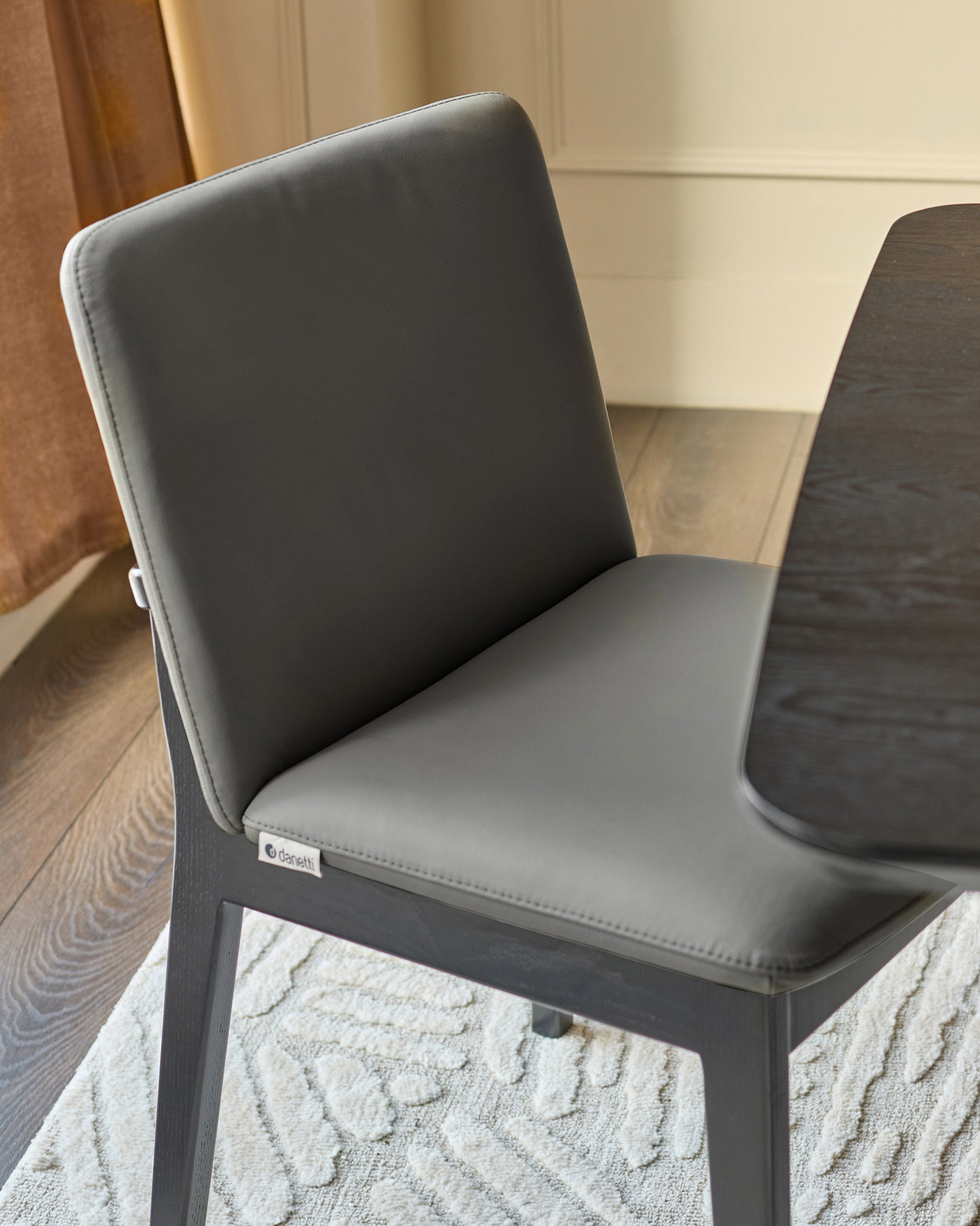 Otis dining chair in dark grey leather, angled side view showing padded seat and backrest on geometric patterned rug.