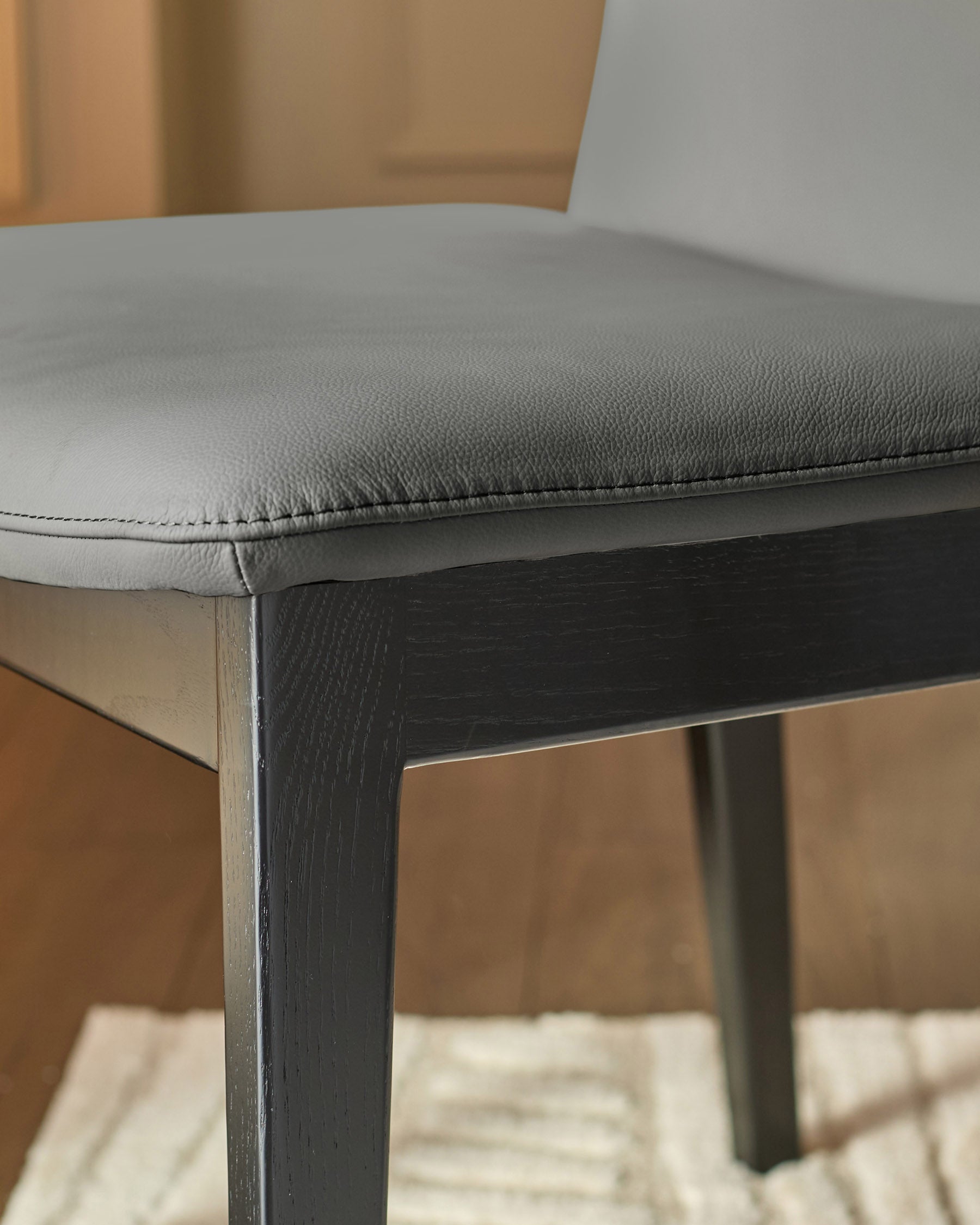Otis dining chair with dark grey wooden legs and light grey leather seat, shown in close-up detail view.
