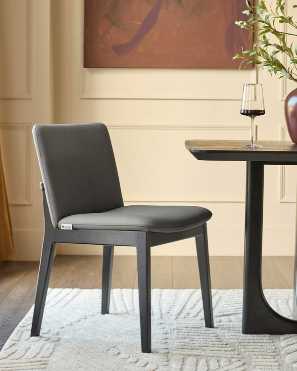 Dark grey leather dining chair with black wooden frame, shown at a round table with wine glass in a modern interior setting.