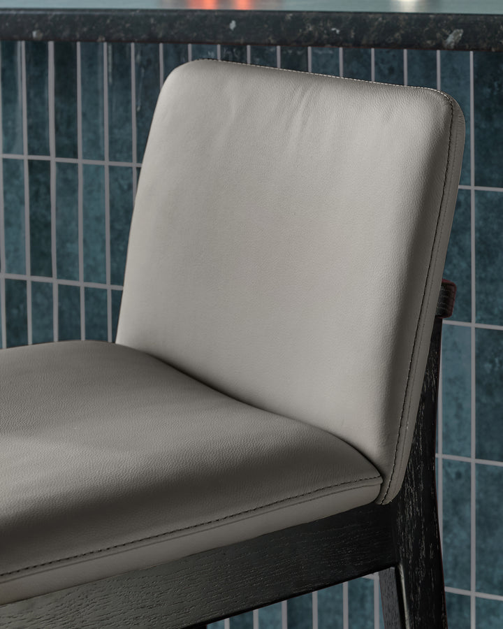 Otis bar stool in dark grey with cream leather seat and backrest, angled side view.