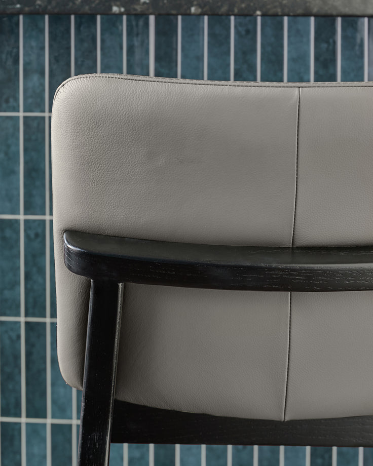 Otis bar stool in dark grey leather with black wooden frame, shown in close-up side view detail.