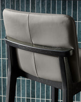 Otis bar stool in dark grey leather with black wooden frame, shown from side angle highlighting the backrest and seat.
