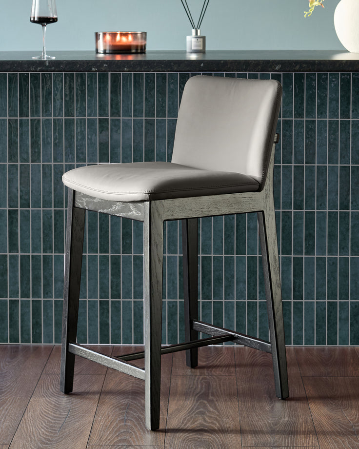 Otis bar stool in dark grey leather with wooden frame, shown against tiled backsplash in modern kitchen setting.