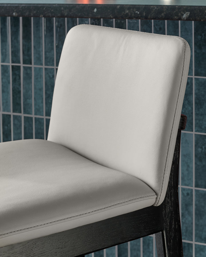 Otis bar stool in light grey leather, close-up side view showing backrest and seat with dark wood frame.