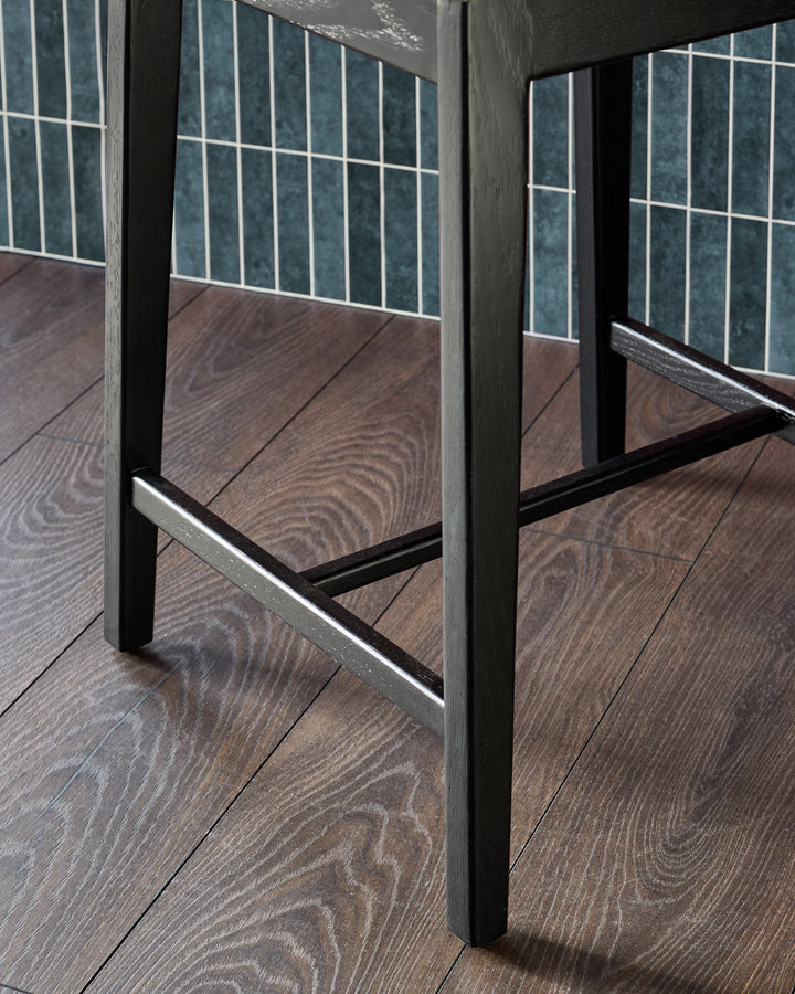 Otis bar stool with black metal frame and footrest, shown from close-up side angle on wood flooring.