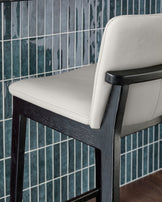Otis bar stool with light grey leather seat and black wooden frame, shown at an angle against tiled backsplash.