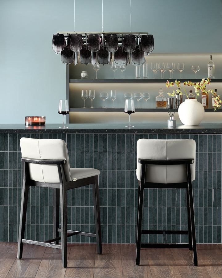 Otis bar stool in light grey leather with black wood frame, shown as pair at modern bar counter.