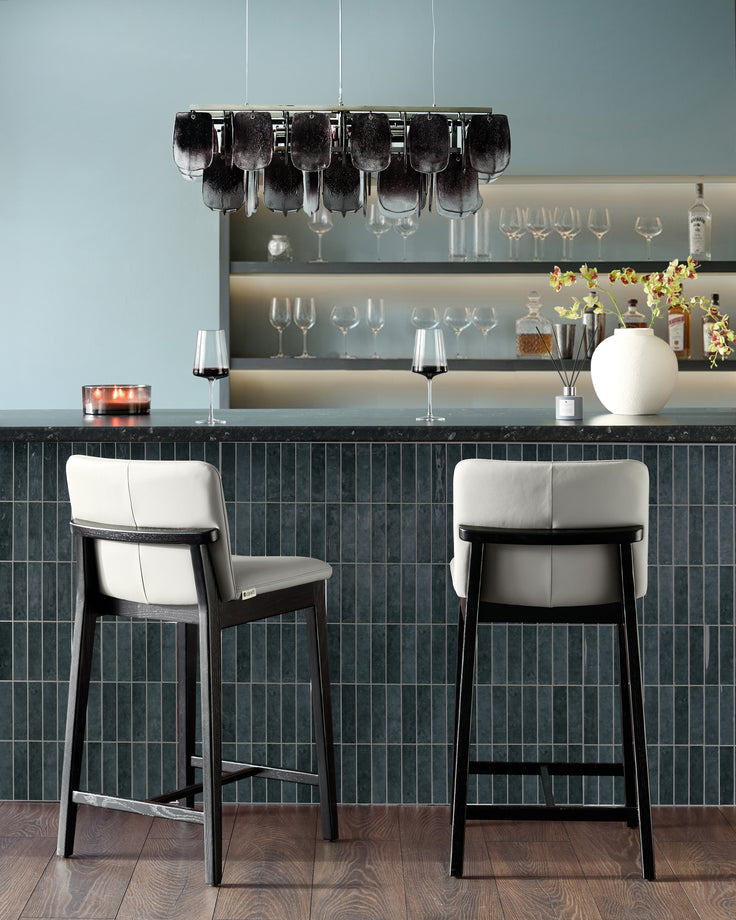 Otis bar stool in light grey leather with black wood frame, shown as pair at modern bar counter.