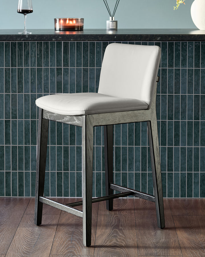 Otis bar stool with light grey leather seat and backrest, weathered grey wood frame, and black footrest.