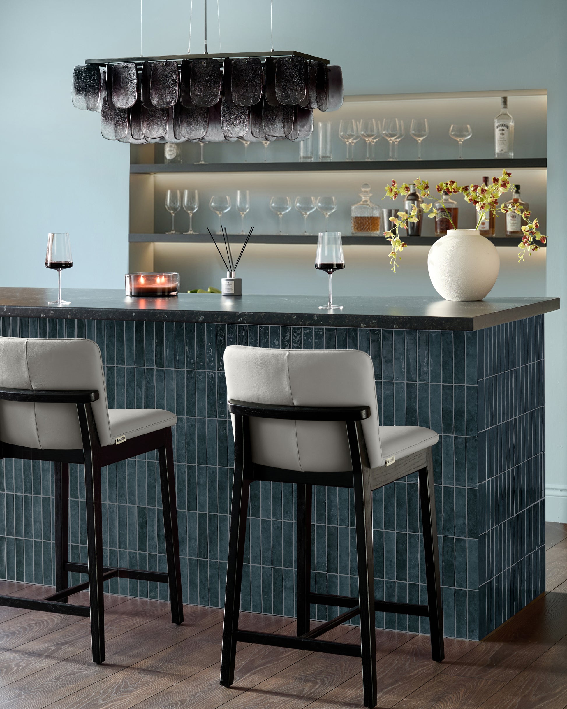 Otis bar stool in light grey leather with black wooden frame, shown at dark teal kitchen island counter.