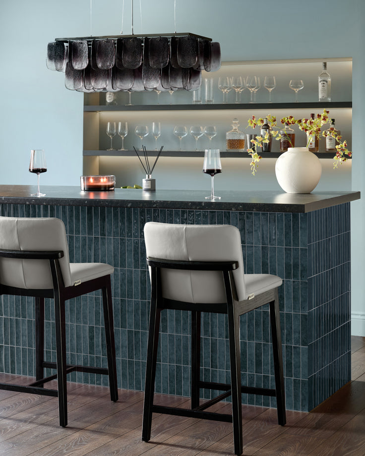 Otis bar stool in light grey leather with black wooden frame, shown at dark teal kitchen island counter.