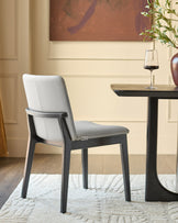 Otis dining chair in light grey leather with black wooden frame, shown at a small black table in a styled room setting.