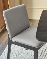 Otis Dining Chair in Light Grey Leather - Side view showing cushioned backrest and seat with dark wood frame on patterned rug.