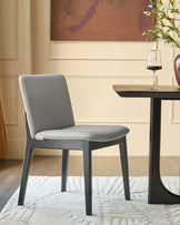 Otis dining chair in light grey leather with dark wood frame, shown in modern room setting next to side table.